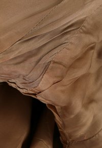 Gros plan d'un tissu brun clair froissé avec une texture de tissage visible et des coutures cousues, montrant des plis et des rides.