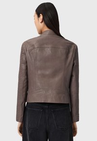 Braune Lederjacke mit gerippten Details an den Schultern. Verfügt über einen taillierten Schnitt und eine glatte Textur, kombiniert mit dunklen Jeans.
