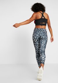 Sostenedor deportivo negro con tirantes entrecruzados y detalle recortado, combinado con leggings ajustados que presentan un patrón abstracto en azul marino y blanco.