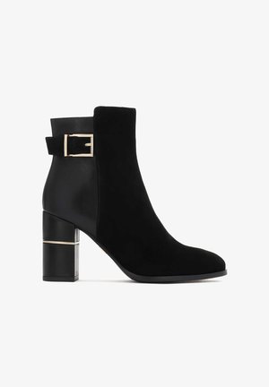 Zwarte suede en leren enkellaars met blokhak en gouden gespdetail aan de zijkant, strak en modern ontwerp.