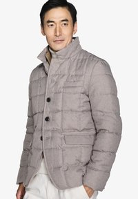Lys grå quilted jakke med ståkrave, der har sorte knapper og to forlommer. Materialet har en blød, struktureret overflade.