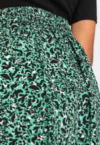 Falda verde y negra con un patrón, cintura fruncida y bolsillos, que presenta una tela texturizada con acentos abstractos en blanco.