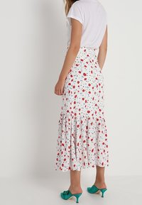Jupe florale blanche avec des motifs de fleurs rouges et bleues, ourlet froncé et silhouette évasée. Associée à un simple haut blanc.