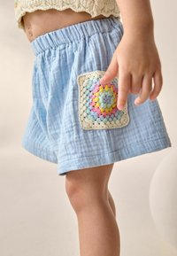 Helleblaue Baumwollshorts mit einem strukturierten Finish und einem auf der Vorderseite angenähten bunten gehäkelten Patch.