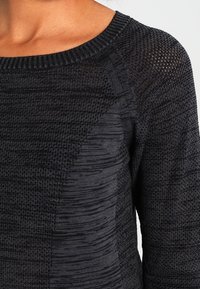 Černý pletený svetr s texturovaným vzorem, širokým výstřihem a žebrovanými okraji. Má různé styly pletení po celé tkanině. Měkký materiál.
