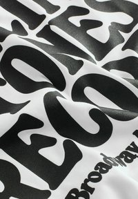 Schwarzer und weißer Stoff mit großen, auffälligen Texten und einer glatten Textur. Der Text beinhaltet "BROADWAY" und abstrakte Formen.