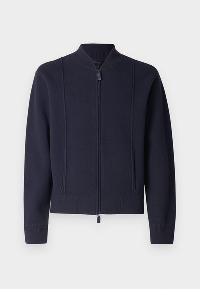Jūrinė zip-up striukė, pagaminta iš minkštos medžiagos, su aukštu apykakle, raštuotais rankogaliais ir dviem priekinėmis kišenėmis. Švarios linijos ir minimalistinis dizainas.