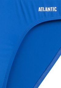 Niebieskie majtki bikini wykonane z fakturowanej tkaniny, z przeszytymi brzegami i słowem "ATLANTIC" nadrukowanym na boku w kolorze białym.