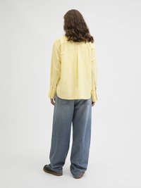 Gul langermet skjorte med en avslappet passform, kombinert med løse denimjeans og mørkebrune sko. Minimalistisk design, ingen synlige mønstre.