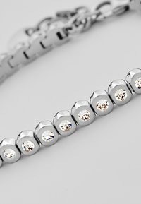 Braccialetto d'argento con gemme trasparenti rotonde incastonate in anelli di metallo circolari, con superficie lucida e chiusura a catena.