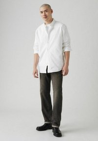 Witte button-up shirt over een witte t-shirt, gecombineerd met donkerwas jeans en zwarte leren laarzen. Eenvoudig, strakke ontwerp.