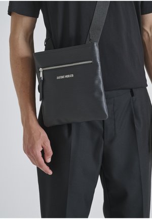 Borsa a tracolla nera realizzata in materiale testurizzato con una tasca frontale con cerniera. Dotata di accessori in argento e logo in rilievo sulla parte anteriore.