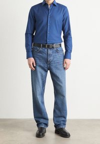Niebieska koszula z guzikami, dżinsy o luźnym kroju, czarny pasek i czarne buty. Gładki materiał koszuli, wyblakłe dżinsy i solidne obuwie.