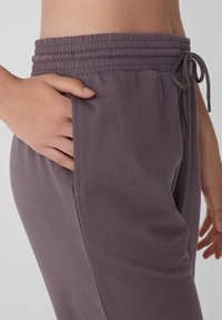 Pantalones de chándal gris oscuro con cintura elástica, cordón y bolsillos laterales. Tejido suave con una textura lisa y un ajuste relajado.