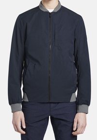 Námořnická bombarďák s šedým límcem, zipem v přední části, bočními kapsami a žebrovanými manžetami. Hladká tkanina s jednoduchým, moderním designem.