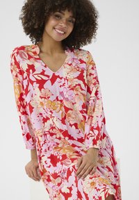 Lilledega punane ja roosa kleit, millel on V-kaelus. Pikkade varrukatega, millel on elastsed mansetid, esitleb kombineeritud suuri ja väikeseid lillemustreid.