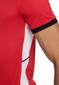 Maglia sportiva rossa con design aderente, caratterizzata da un pannello in rete bianco e rifiniture nere sulle maniche. Texture liscia e maniche corte.