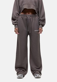 Bruine, brede sweatpants gemaakt van zachte stof met een elastische tailleband, voorzien van een trekkoord en zijlogo-detail.