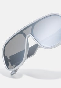Lunettes de soleil avec une élégante monture argentée, de grandes verres gris dégradé, et un design épuré comportant un pont courbé et des accents latéraux subtils.