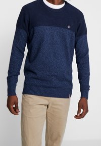 Dunkelblauer strukturierter Pullover mit gerippten Bündchen und Saum. Verfügt über einen hellblauen oberen Abschnitt und ein kleines Logo auf der Brust.