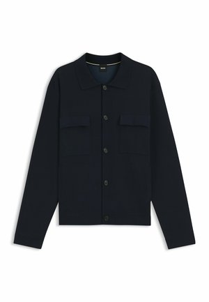 Schwarze Hemdjacke mit langen Ärmeln, Knopfleiste, Kragen und zwei Brustklappentaschen, flach liegend auf weißem Hintergrund.