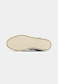 Sneaker nera con suola testurizzata, dotata di una suola in gomma beige e parte superiore liscia. Il design è minimale, senza motivi o accenti visibili.