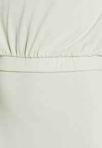 Ljust grönt tyg med en mjuk textur; har sammetslena detaljer längs toppen och ett slätt midjeband nedanför.