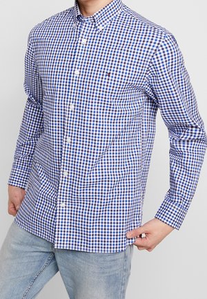 Camisa de vestir de cuadros vichy en azul y blanco, con mangas largas, cuello abotonado y un logo en el pecho, hecha de tela de algodón.
