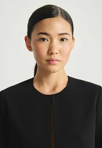 Vêtement noir structuré avec un col rond et une ouverture subtile à l'avant. Texture de tissu lisse avec un design minimaliste.