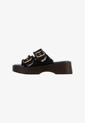 Sandale à plateforme noire avec deux lanières en tissu effiloché et boucles dorées, dotée d’une semelle à texture bois et d’une légère découpe à la voûte plantaire.