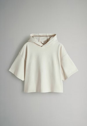 Kurz geschnittener Hoodie in hellem Beige, mit weicher Textur, breiten kurzen Ärmeln und großer Kapuze mit Frontöffnung.