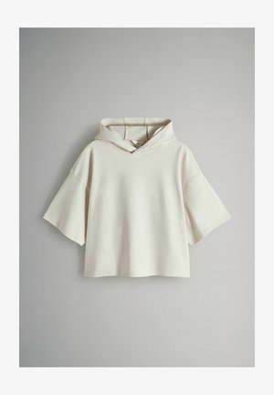 Kurz geschnittener Hoodie in hellem Beige, mit weicher Textur, breiten kurzen Ärmeln und großer Kapuze mit Frontöffnung.