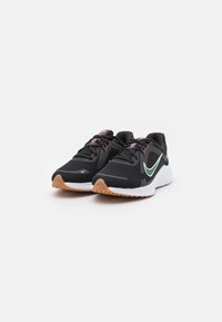 Black athletic shoes with a cushioned white sole and gum-colored accents. Features a textured upper and a prominent green swoosh logo.