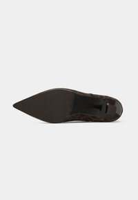 Zapato de tacón alto con punta afilada, parte superior de estampado de leopardo marrón, suela negra lisa y diseño de tacón delgado.