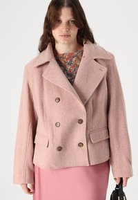 Roosa hundstooth mustriga topeltkootud jakk, millel on suured nööbid, nurgelised kraed ja küljetaskud. Sile villataoline tekstuur. Pikad varrukad.