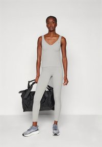 Canotta atletica grigia e leggings in materiale elasticizzato. La modella tiene una borsa da palestra nera e indossa sneakers grigie con dettagli testurizzati.