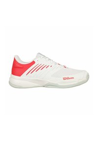 Zapatilla deportiva blanca con acentos rojos, paneles de malla para ventilación y una suela acolchada. Presenta el logo "Wilson" en rojo.