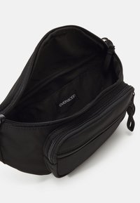 Pochette noire zippée avec deux compartiments, l’un ouvert montrant une étiquette en tissu avec l’inscription "even&odd" à l’intérieur.