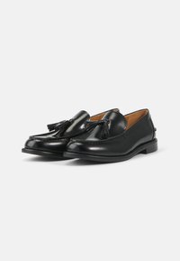 Schwarze Lederloafers mit glatter Oberfläche, Quastenakzenten an der Vorderseite und einem niedrigen, gestapelten Absatz. Dekorative Nähte entlang der Kanten.