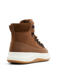 Botas altas marrones hechas de cuero y ante, con ojales negros, cierre de cordones, una entresuela blanca y una suela de goma texturizada.