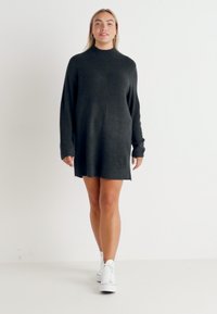 Dark grey oversized sweater dress, featuring a high neckline, long sleeves, and ribbed texture, paired with white sneakers.