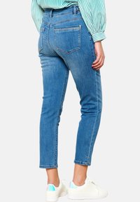 Ohut sininen farkut, joissa on keskikorkea vyötärö, takataskut ja siisti viimeistely, yhdistettynä valkoisiin tennareihin, joissa on kimaltavia yksityiskohtia.