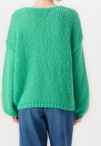 Pull en maille oversize vert avec une finition texturée et duveteuse, doté d'épaules tombantes et d'un col rond, associé à un jean bleu.