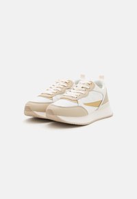 Zapatillas deportivas en beige y blanco con una parte superior texturizada, cierre de cordones, una franja de acento dorado y un diseño de suela acolchada.