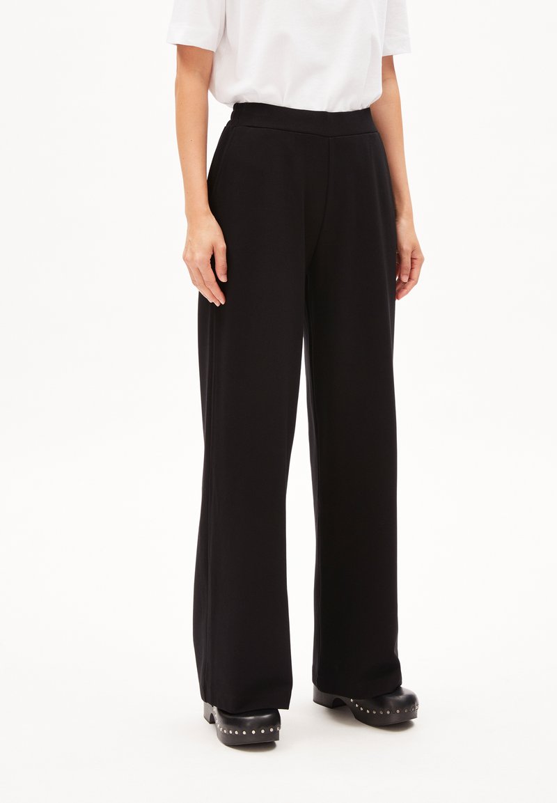 Pantalons larges noirs avec une taille haute et un tissu lisse et extensible. Portés avec des chaussures à plateforme noires ornées de clous argentés.