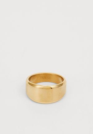 Bague couleur or avec une finition lisse et polie. Présente un anneau plat et le logo gravé "GUESS" à l'intérieur. Design simple.