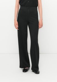 Pantalons larges noirs avec des rayures verticales blanches, fabriqués dans un tissu lisse, présentant une taille haute et une coupe ajustée.