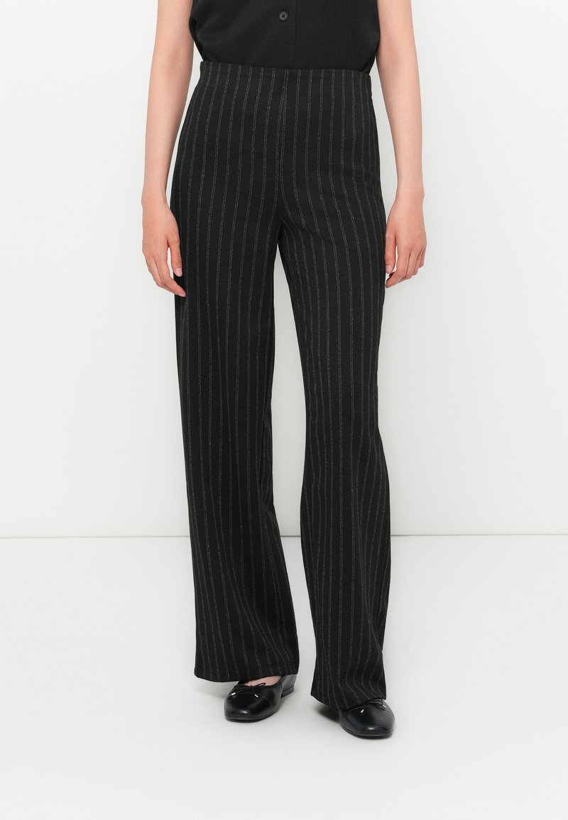 Pantalons larges noirs avec des rayures verticales blanches, fabriqués dans un tissu lisse, présentant une taille haute et une coupe ajustée.