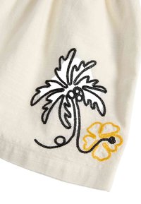 Geborduurd top met een zwarte palmboom en een gele bloem op een gestructureerde crèmekleurige achtergrond. De stiksels belichten de details van het ontwerp.