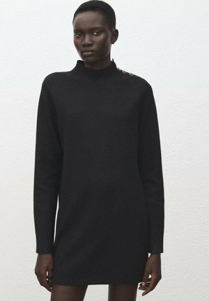 Black knitted dress with a high neckline, long sleeves, and a ribbed hem. Features decorative buttons on the shoulder. Textured fabric.